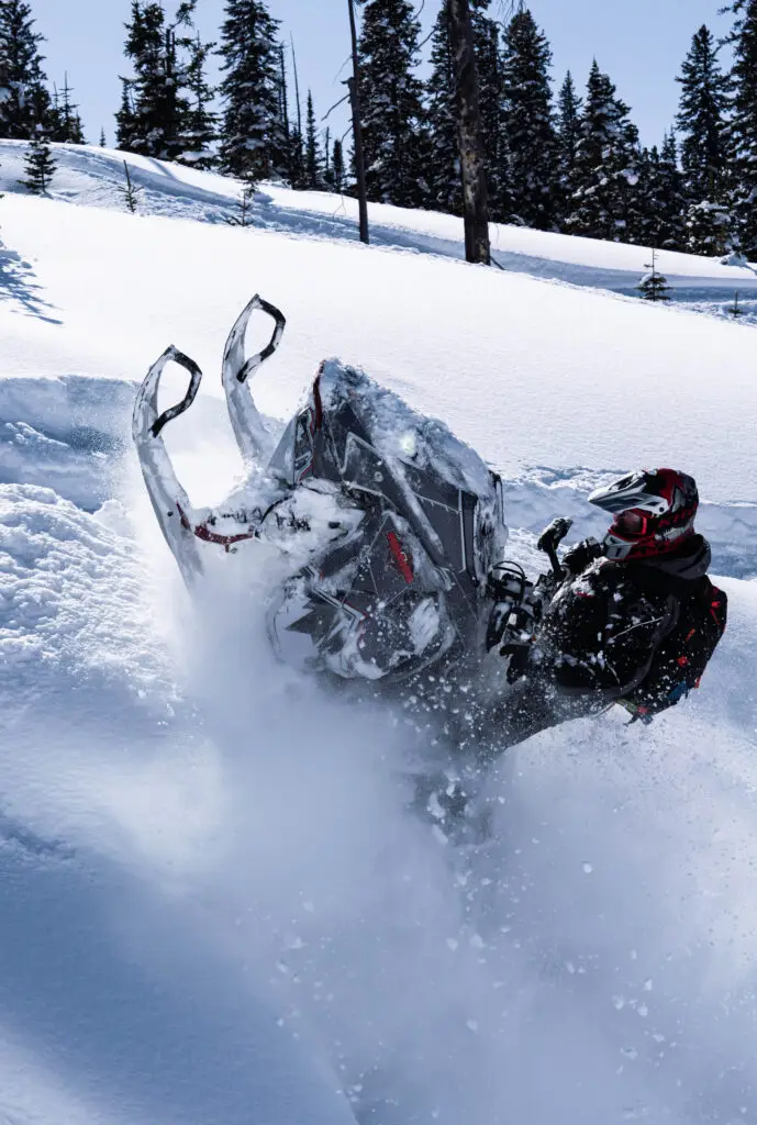 Snowmobile and rider rides up steep snowcovered hill