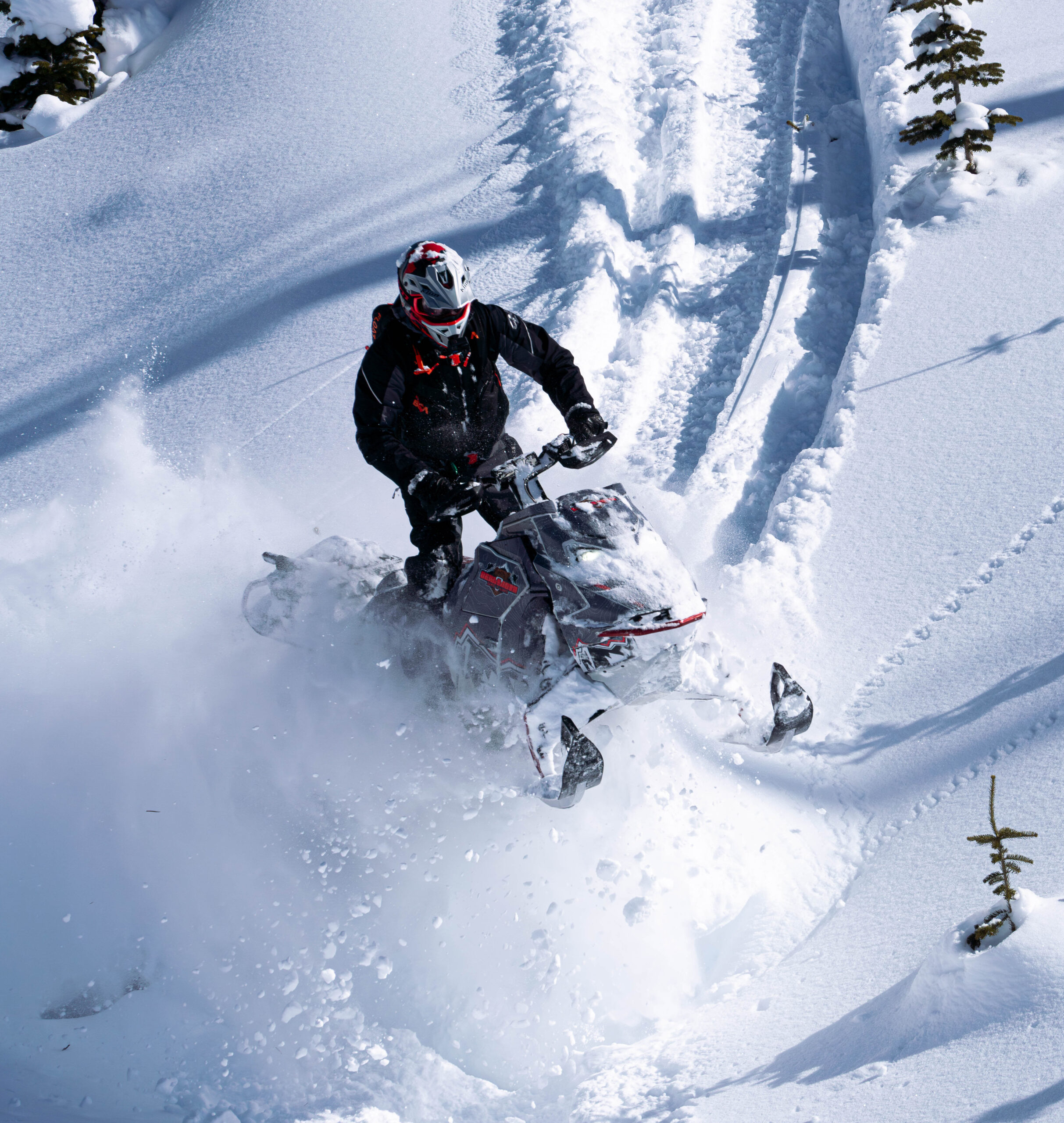 Snowmobile and rider riding down a hill covered in fresh snow